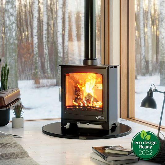 Henley Willow 6.5kW Multi Fuel Eco Stove with roaring fire, set on black hearth in snowy woodland interior